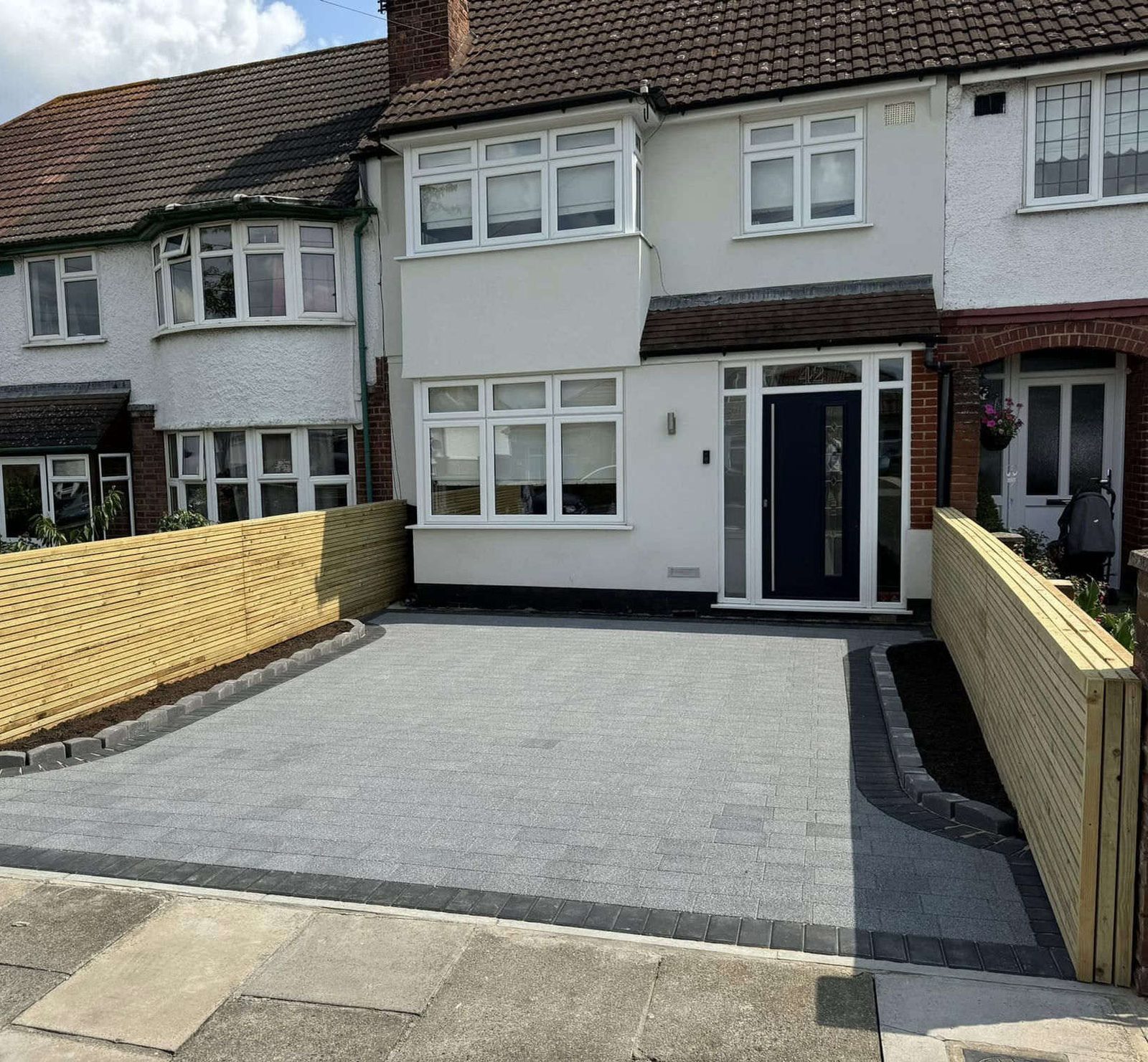 Terraced house with a new grey block paving driveway and timber slat fencing