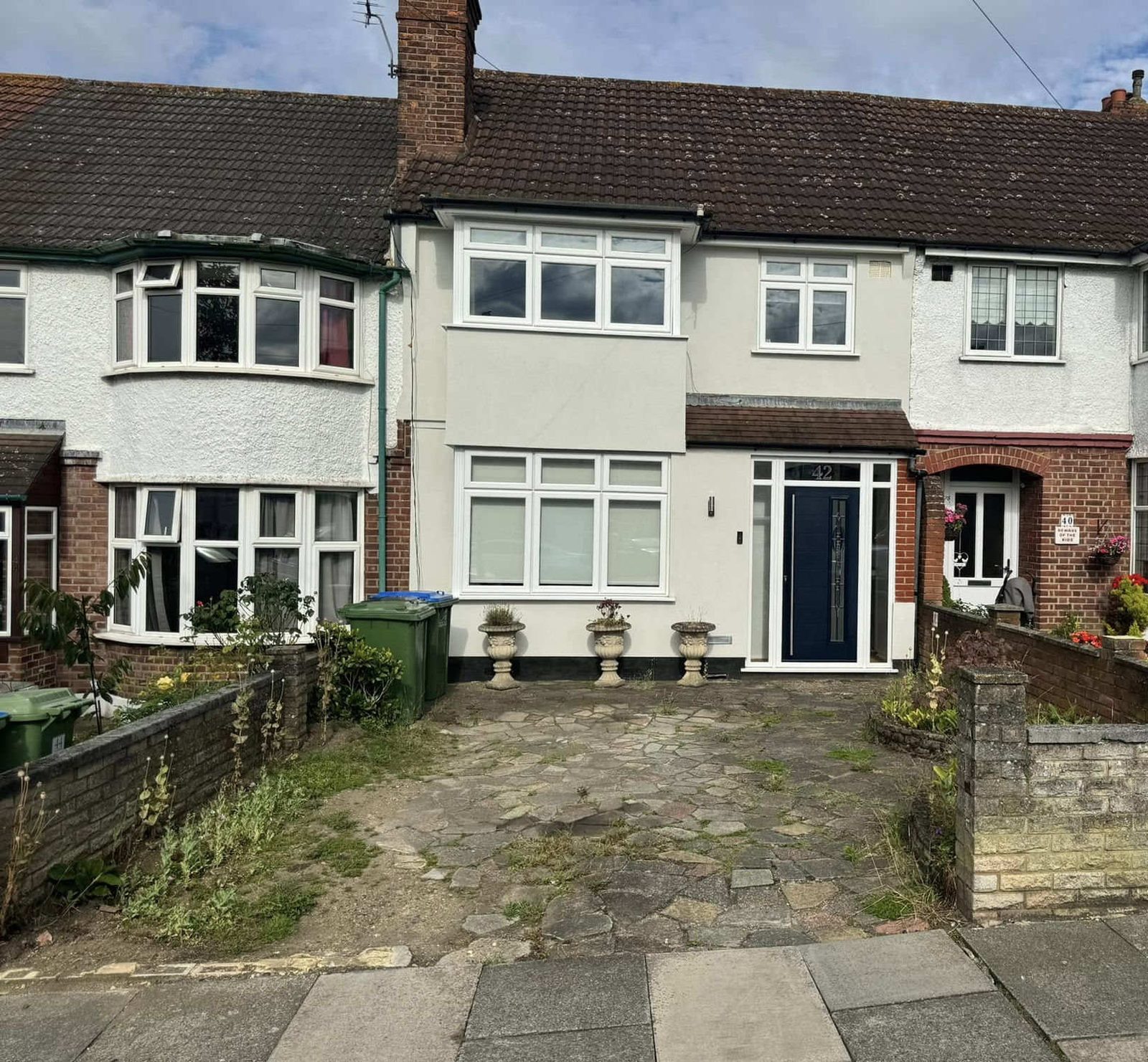Terraced house with a cracked crazy paving driveway and a low front wall