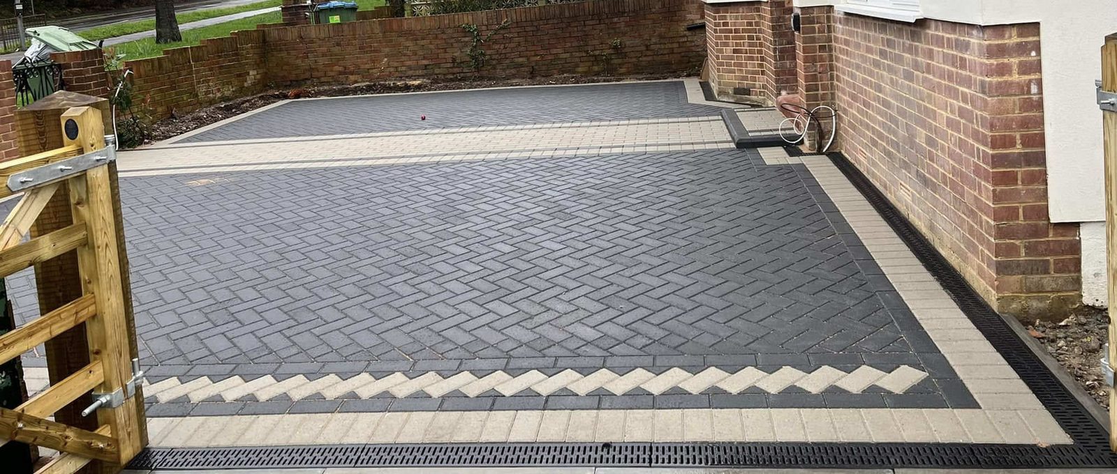 Charcoal herringbone block paving with a buff chevron border and a drainage channel