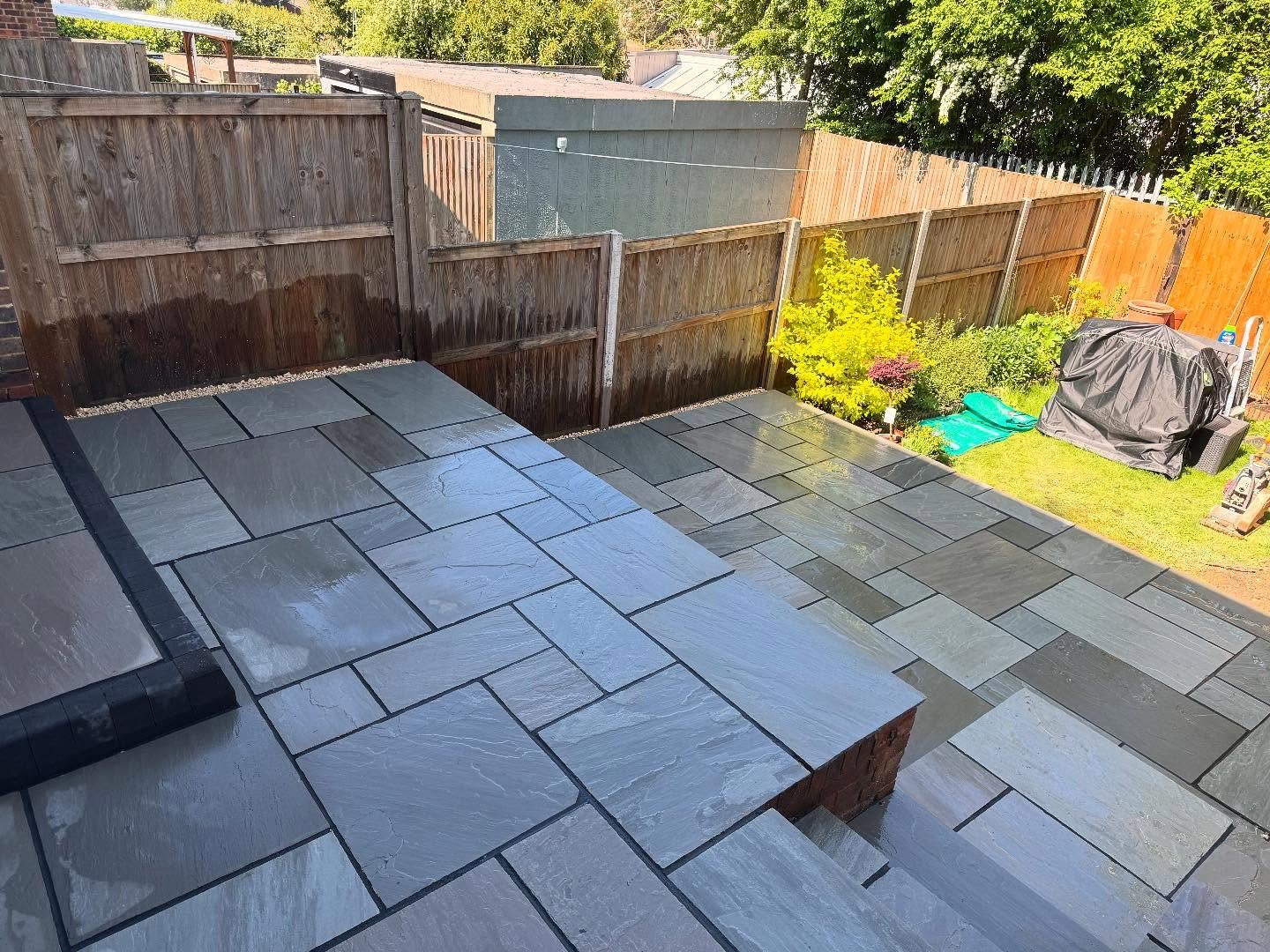 Grey Indian sandstone patio laid across a garden with a brick edged step