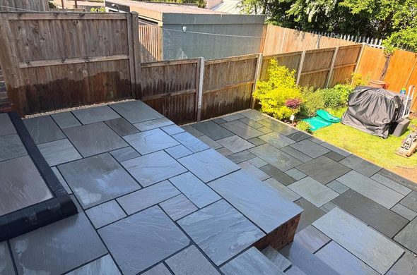 Grey Indian sandstone patio laid across the same garden with a brick edged step