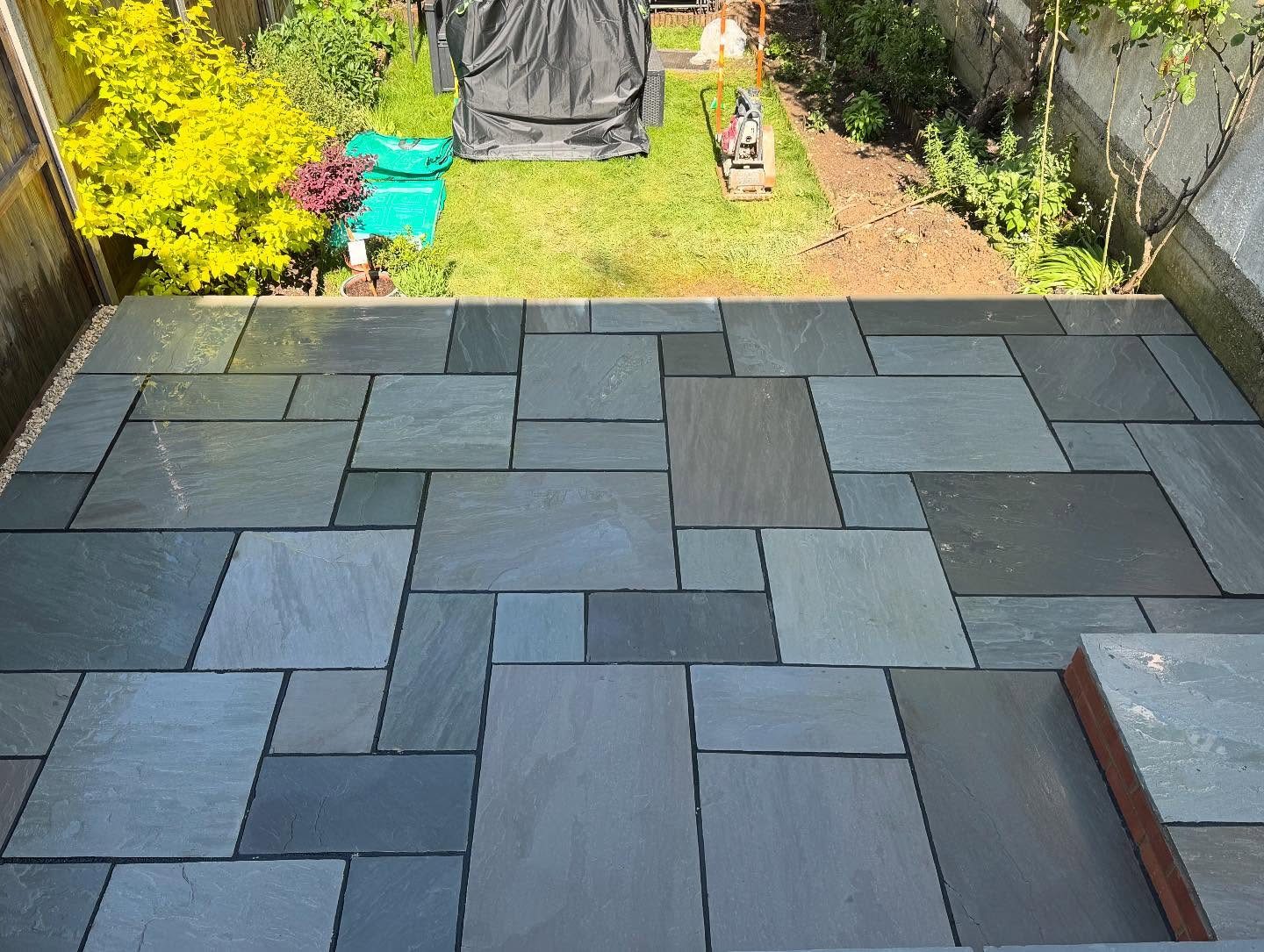 Grey riven sandstone patio seen from above with the lawn and borders behind