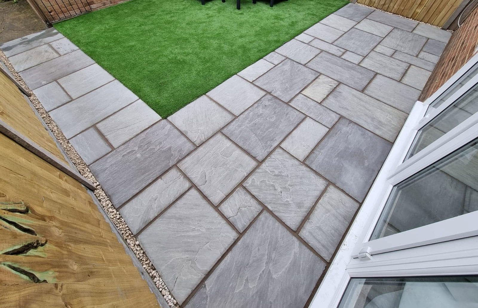 Overhead view of a sandstone patio, gravel border and a square of artificial grass