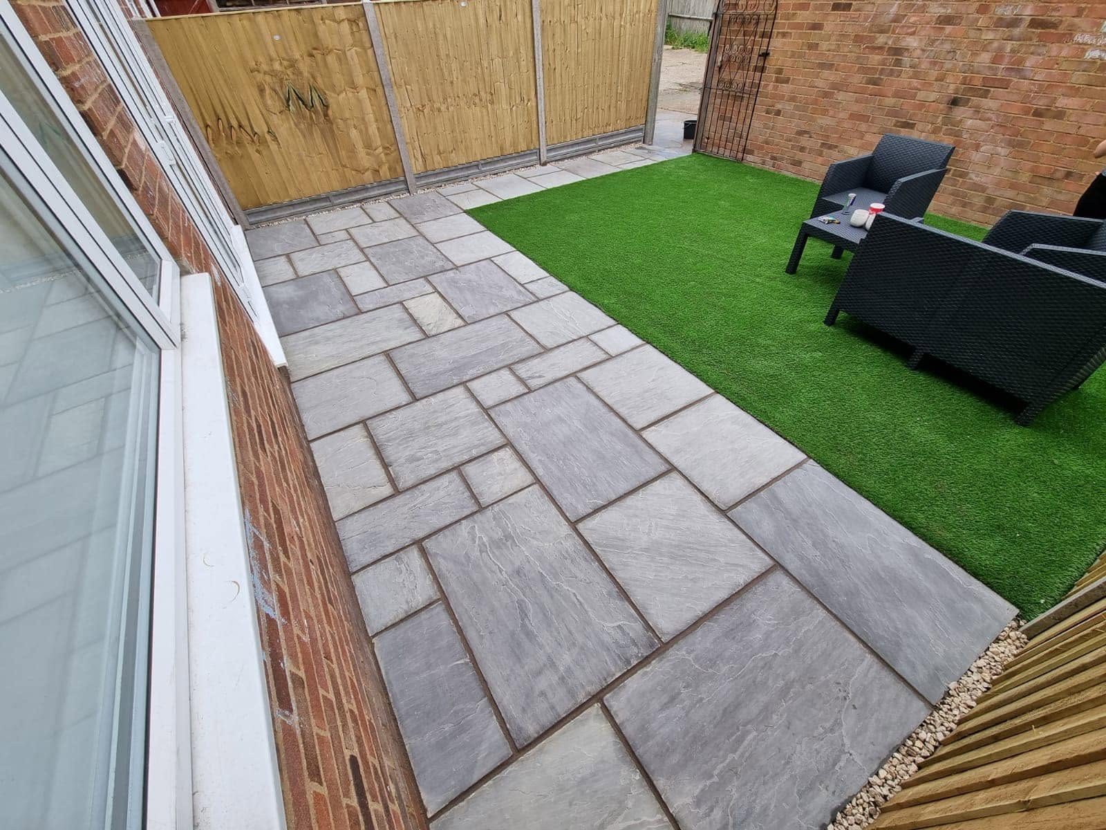 Grey sandstone patio beside a square of artificial grass with rattan furniture