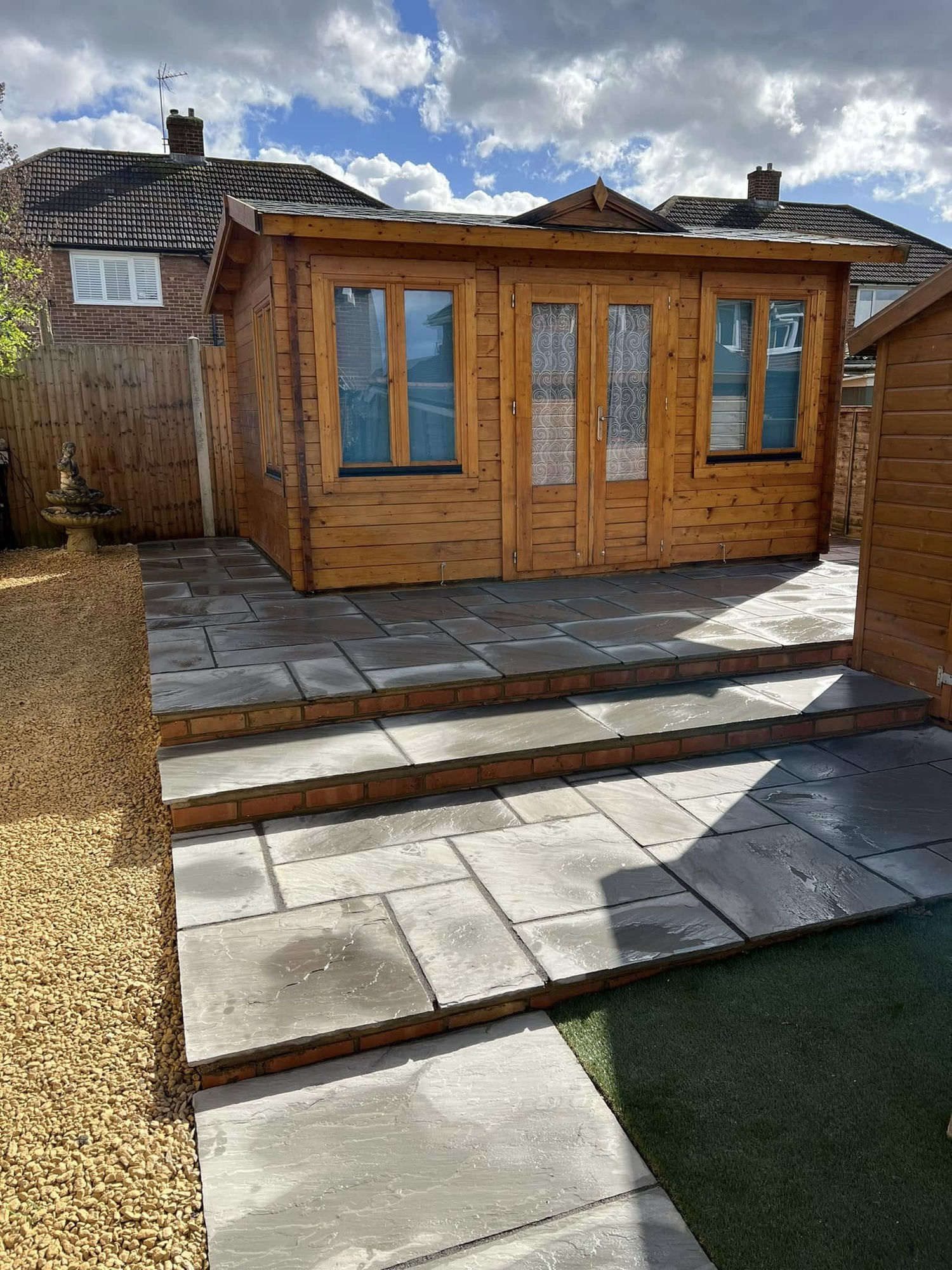 Indian sandstone patio and brick edged steps up to a timber summerhouse