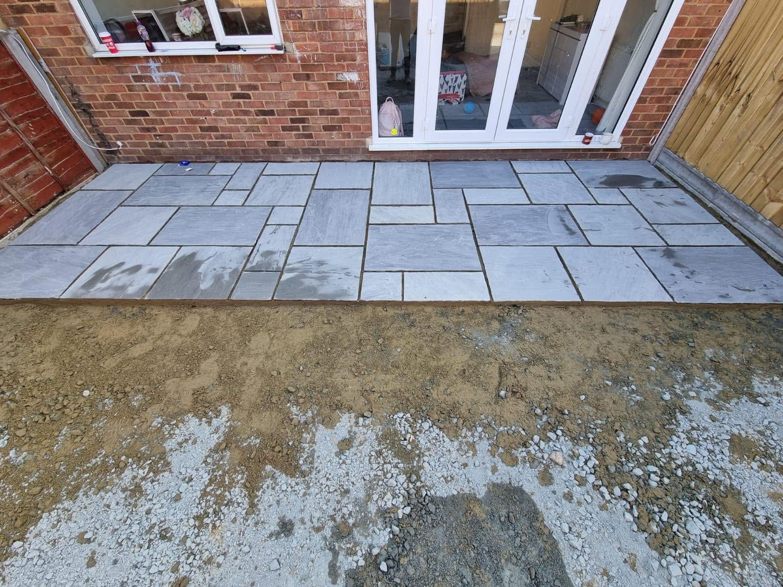 Sandstone slabs being laid on the sand and sub-base against the back of the house