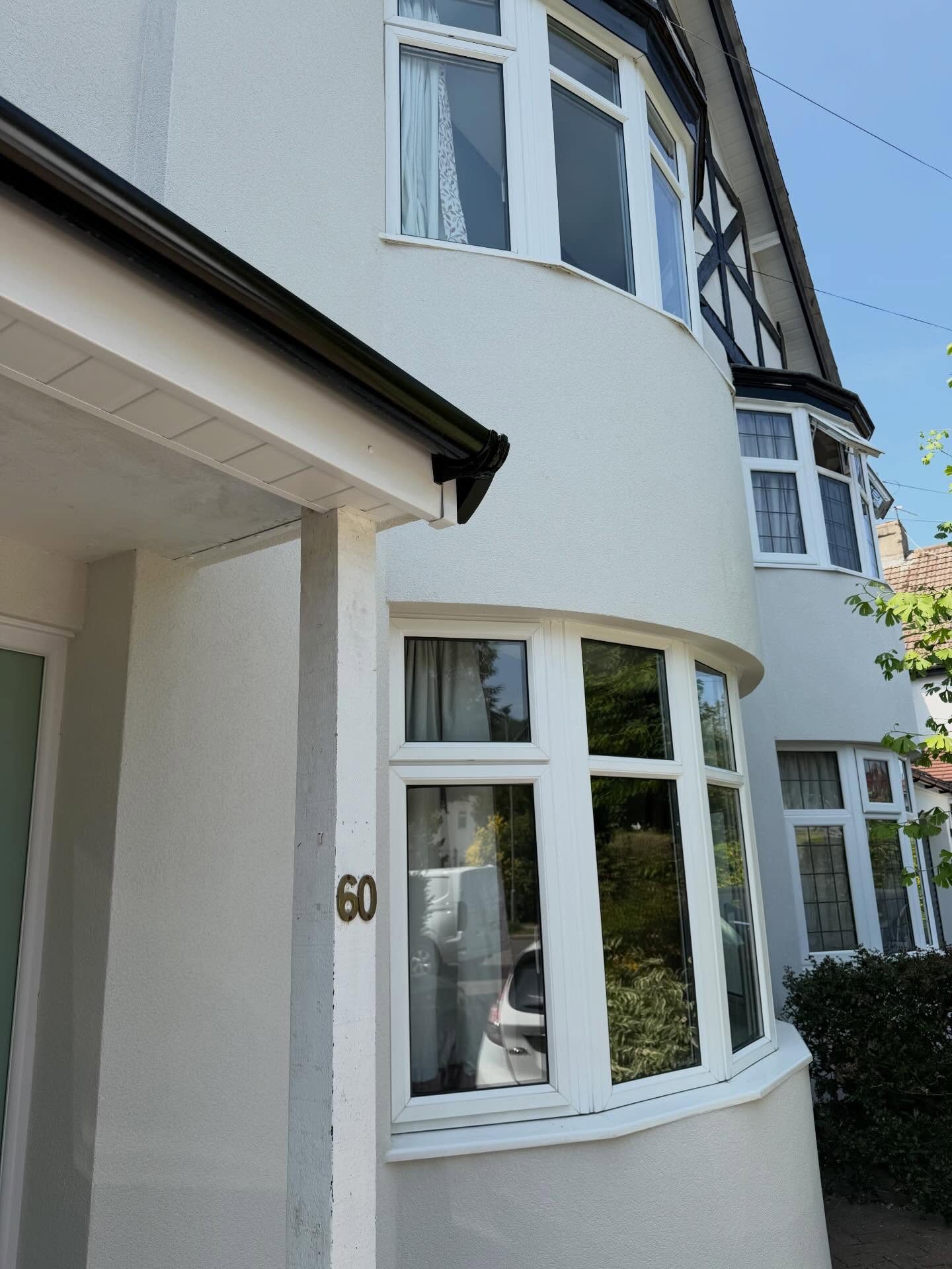 Black UPVC guttering and white windows against a rendered curved bay