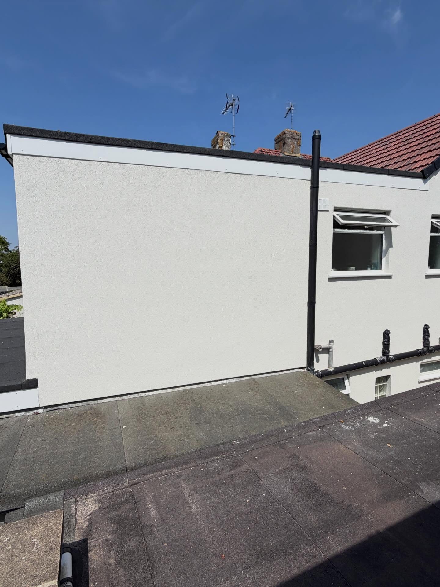 Freshly rendered flat roof extension gable seen from the roof with blue sky behind
