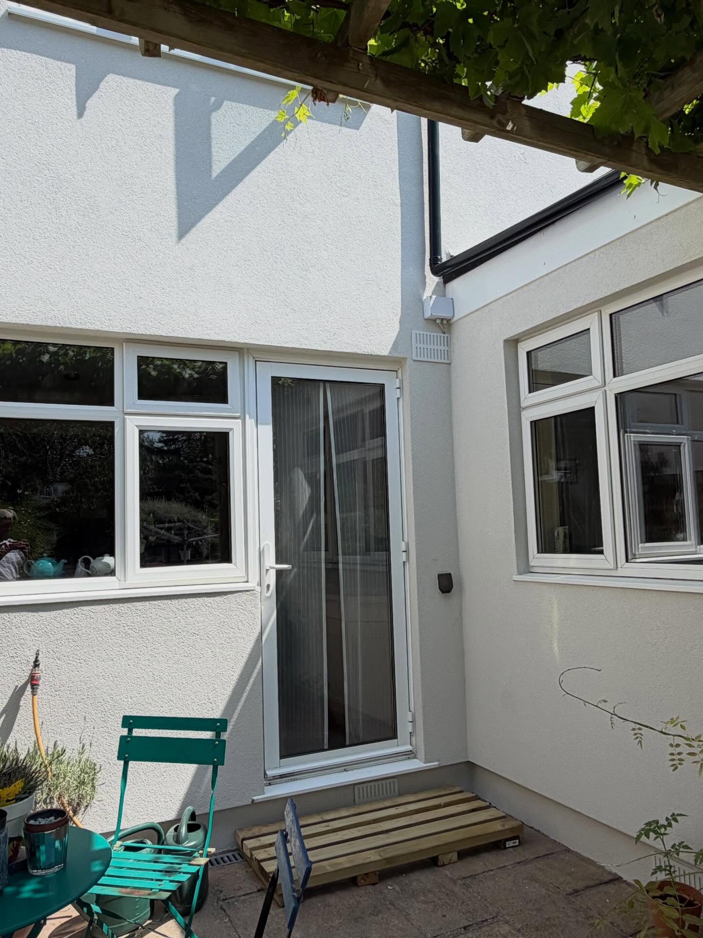 Side return finished in silicone render with a white back door and a small patio