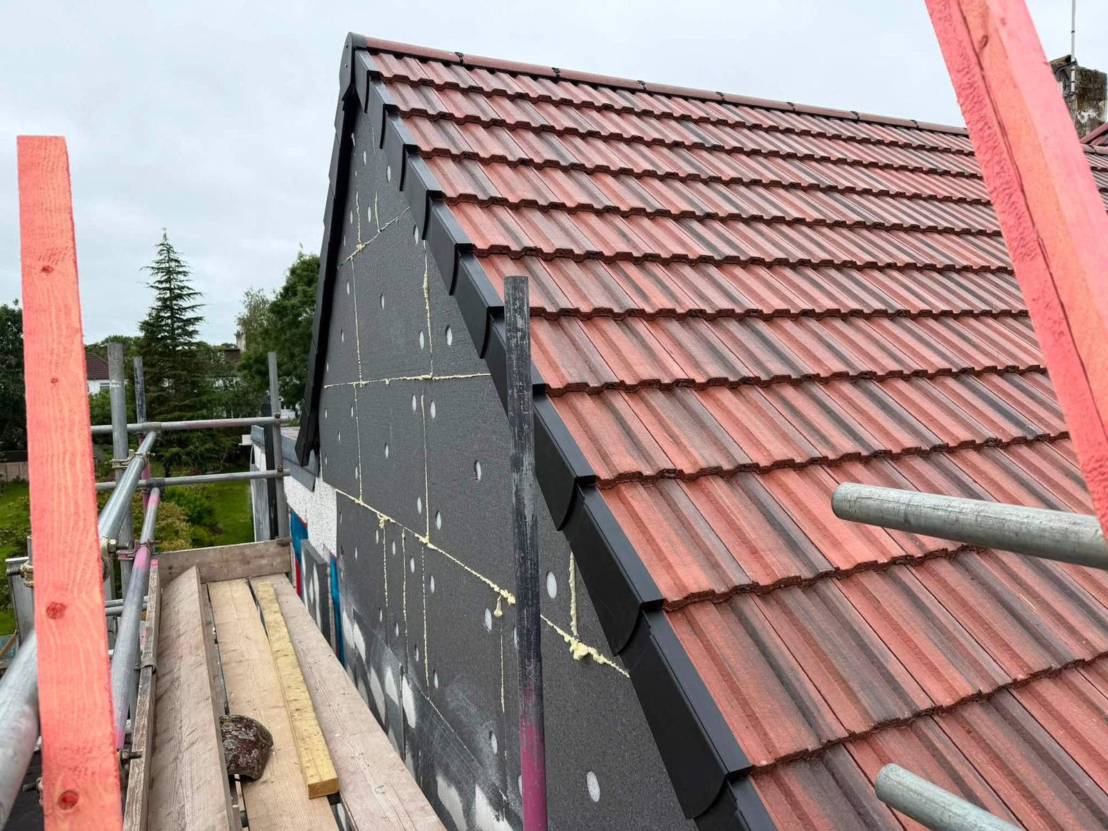 New roof tiles and black dry verge beside a gable covered in insulation boards