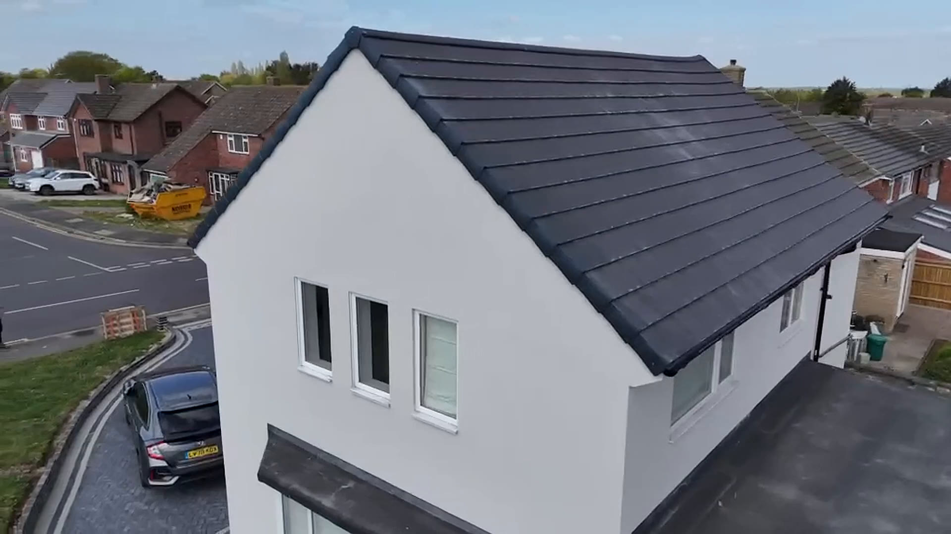 Aerial view of a house finished in white silicone render with a new dark grey tiled roof and a new block paving driveway